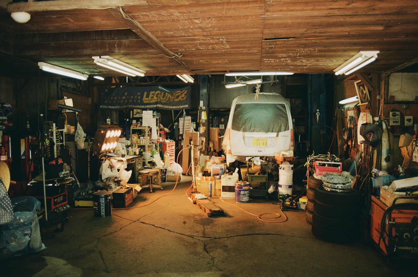 A white van sits on a hydraulic lift inside an auto shop.